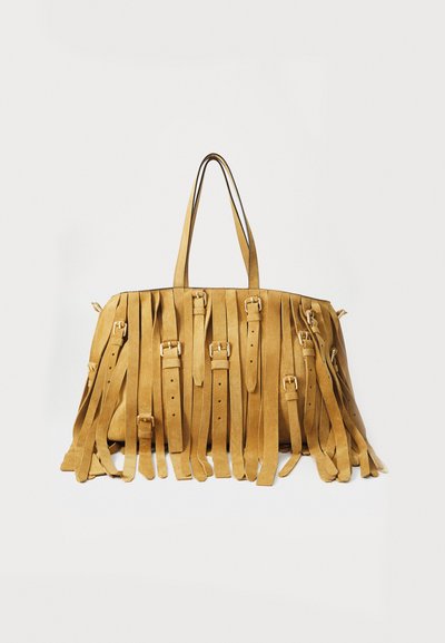Sac en daim beige avec des franges longues, deux poignées supérieures et des boucles en métal. Texture lisse et forme rectangulaire avec un intérieur spacieux.