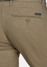 Kaki broek met een gladde textuur, een enkele achterzak met knoopsluiting en een klein merklabel nabij de tailleband.