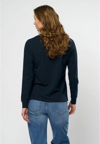 Langermet marineblå skjorte laget av mykt stoff, med rund halslinning og tettsittende mansjetter, kombinert med høyt liv lys blå denim bukser.
