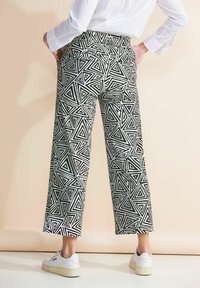 Pantalons larges à motifs noir et blanc avec un design géométrique en triangles, dotés de poches et d'une taille haute, associés à des baskets blanches.