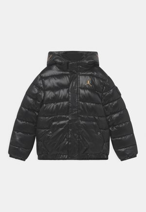 Chaqueta acolchada negra con capucha, textura brillante, acolchado horizontal, bolsillos frontales y un logo dorado en el pecho.