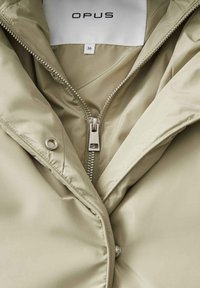 Giacca puffer verde chiaro con chiusura a zip, hardware argentato e texture liscia. Etichetta con la scritta "OPUS", taglia 36.