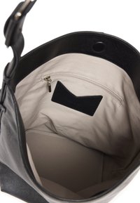 Intérieur d'un sac à main en cuir noir avec une doublure en tissu beige, comprenant une poche zippée et une étiquette en cuir noir. Texture lisse, design ouvert.