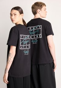 Czarne bawełniane koszulki z grafiką z logo "TOMMY JEANS" i turkusowymi akcentami. Krótkie rękawy i luźny krój. Prosty okrągły dekolt.