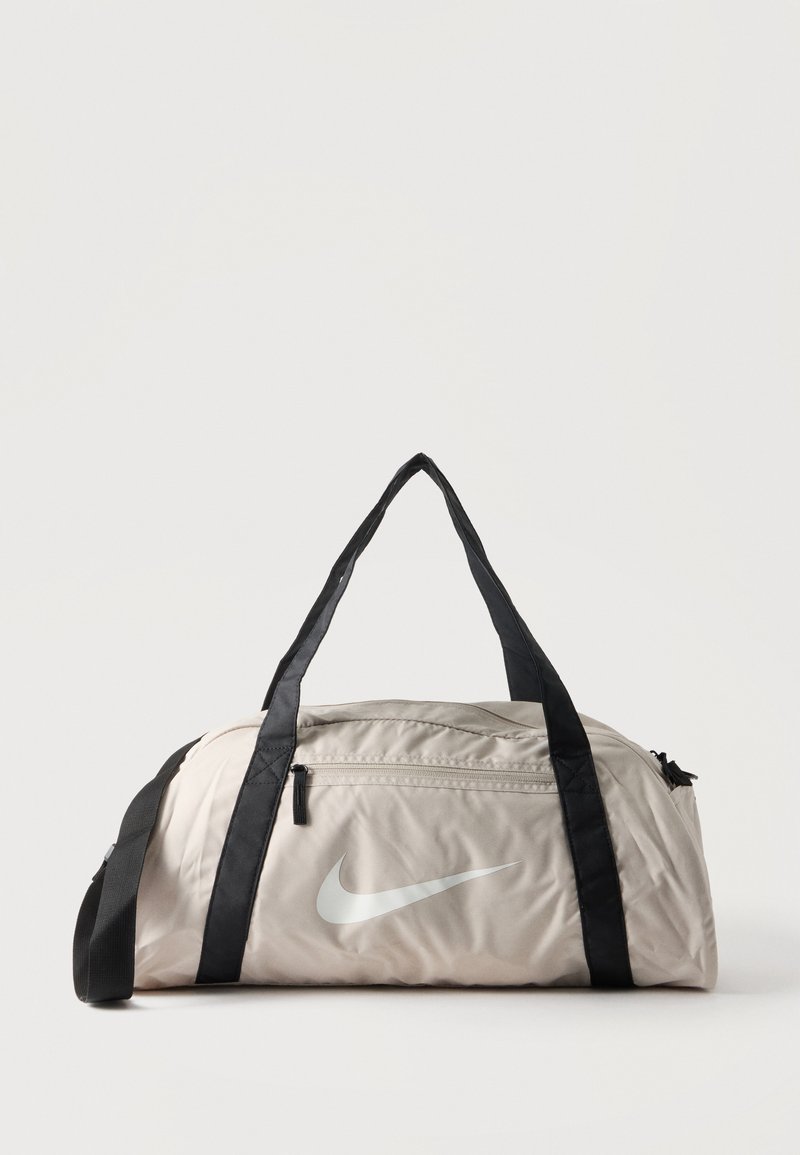 Φως μπεζ σάκος duffel Nike με μαύρες λαβές, μπροστινή τσέπη με φερμουάρ και λευκό λογότυπο swoosh σε απλό ανοιχτό φόντο.