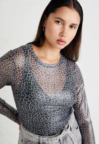 Gray long-sleeve top made of sheer mesh fabric with a black leopard print pattern and a scoop neckline. Pairing gray high-waisted pants is visible.