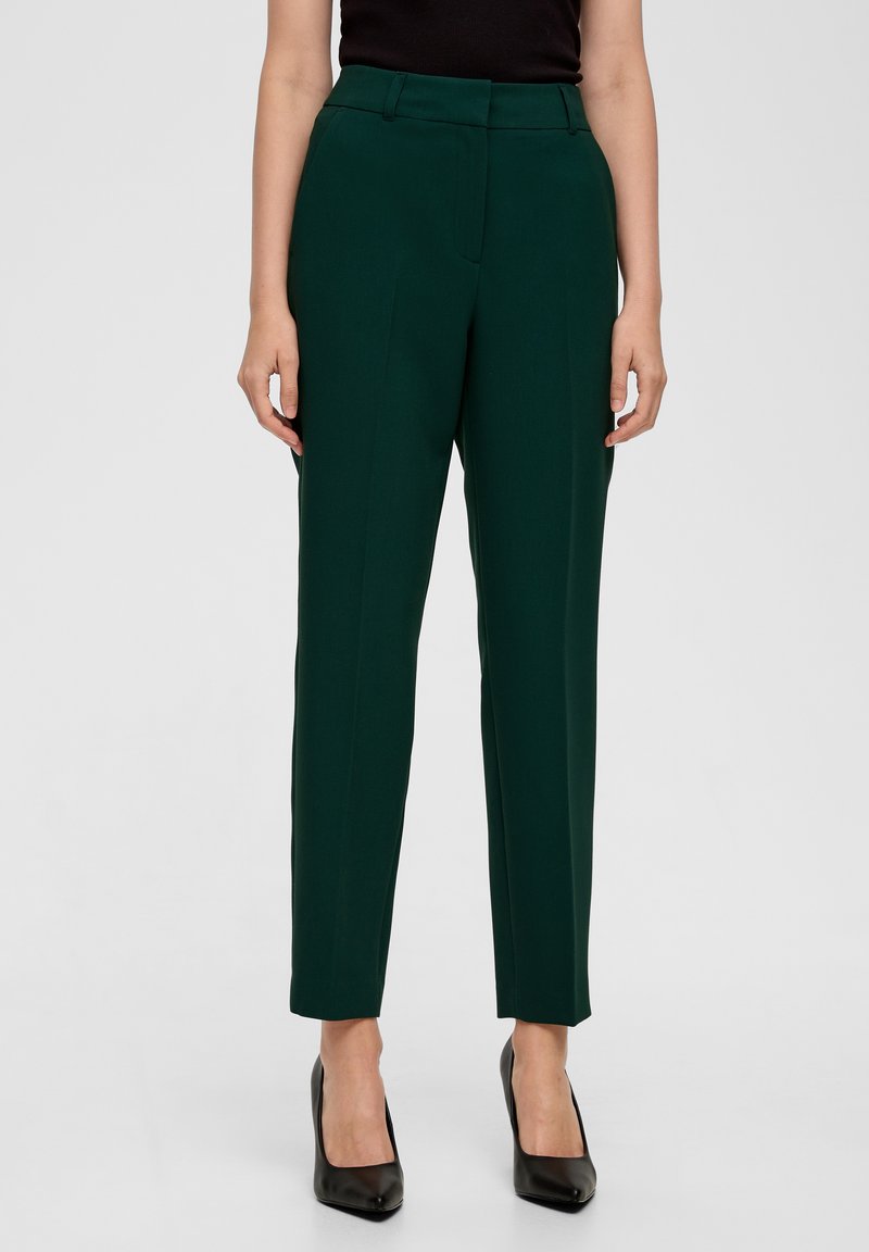 Pantalon vert sur mesure avec une taille mi-haute, des jambes droites et deux poches avant, associé à des talons hauts noirs. Tissu tissé lisse.