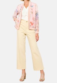 Ljusrosa bomberjacka med blommönster, vit topp med twistdetalj, krämfärgade vida byxor och gyllene klacksandaler.