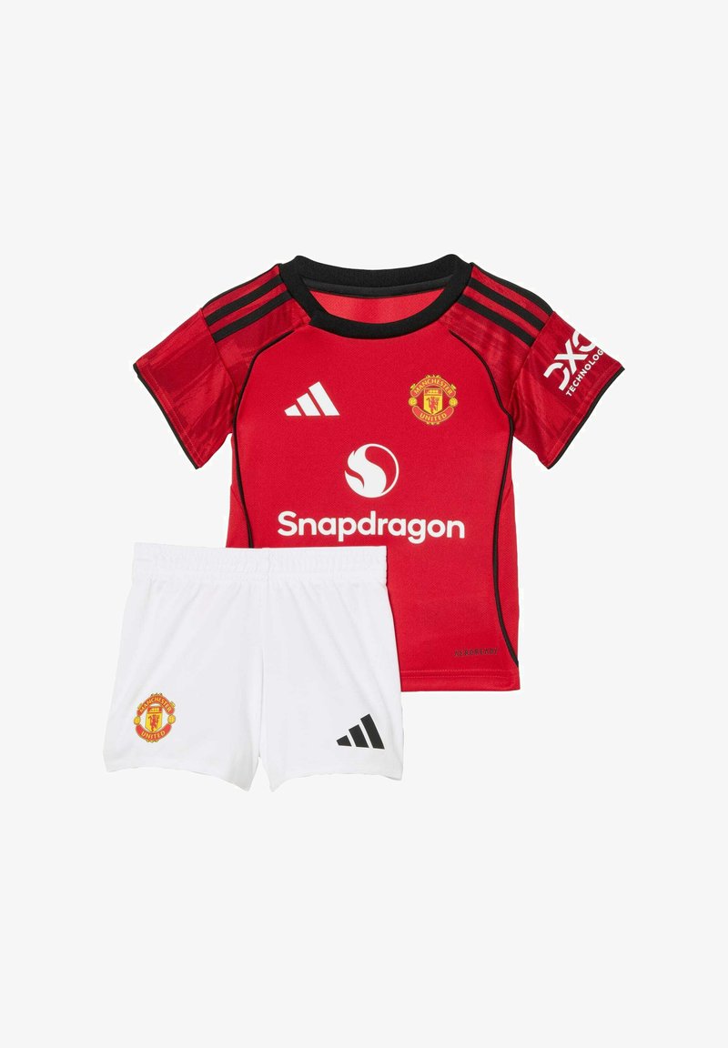 Crvena nogometna majica Manchester Uniteda s crnim detaljima, bijele hlače s crnim Adidas prugama i logotipima kluba. Izrađena od prozračnog materijala.