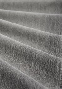 Szary materiał z wyraźnym skośnym splotem tkackim, ukazujący teksturowaną powierzchnię i subtelny połysk. Ujęty w miękkich fałdach, podkreślających głębokość i warstwowość.