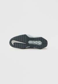 Σόλα αθλητικού παπουτσιού Nike με μαύρη επιφάνεια πρόσφυσης, διαφανή αερόσακο κοντά στη φτέρνα και μεγάλο λευκό λογότυπο swoosh σε ανοιχτό γκρι φόντο.