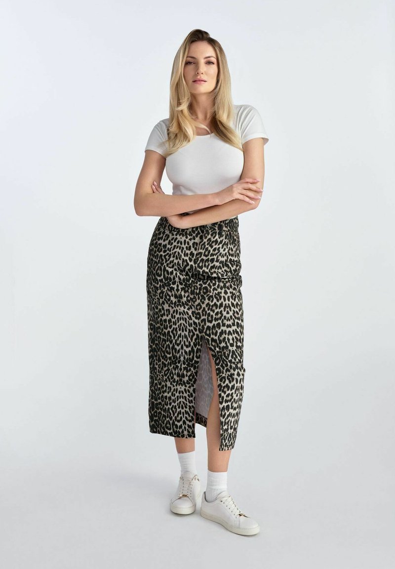 Spódnica midi w panterkę z rozcięciem bocznym, wykonana z gładkiego materiału, w zestawieniu z białą bluzką z krótkim rękawem i białymi trampkami. Neutralne tło.