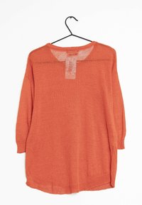 Pull en tricot orange sur un cintre noir, avec des manches longues, un col rond et une coupe loose avec des fentes sur les côtés. Tissu légèrement texturé.