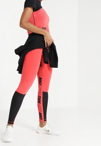Czerwony i czarny strój sportowy z krótkim topem i legginsami z wysokim stanem, z logo "Nike" i dopasowanym krojem. Białe sneakersy.