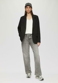 Schwarzes Blazer, weißes Oberteil mit Spitzenbesatz, graue ausgestellte Jeans, silberne Sneakers und graue Mütze. Glatter Stoff, maßgeschneiderter Schnitt und eine lässige Passform.