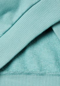 Tessuto blu chiaro con una texture liscia, caratterizzato da un orlo a coste e due diversi modelli di maglia, creando profondità visiva e contrasto.