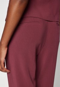 Bordeaux skräddarsydda byxor med en slät yta, som har en sidoficka och diskreta sömmar, utformade för en figurnära passform.