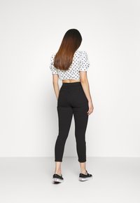 Svarta skinny jeans med hög midja och lätt stretch, kombinerat med en kortärmad vit topp med prickar. Minimalistisk design och smickrande silhuett.