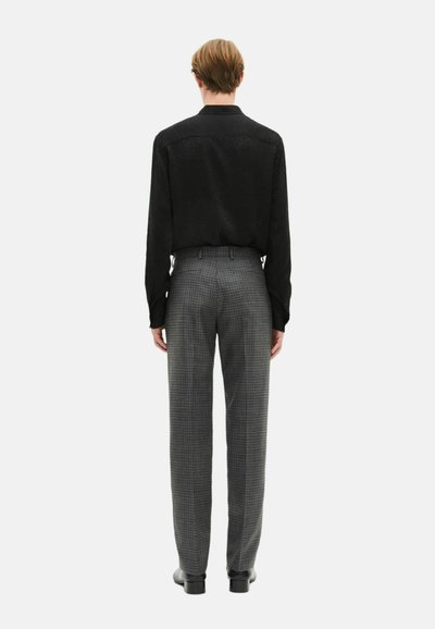 Czarna koszula z długim rękawem w połączeniu z szarymi spodniami w kratę. Materiał wygląda na gładki; spodnie mają dopasowany krój z prostą nogawką.