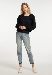 Zwart getextureerd topje met pofmouwen, ronde halslijn en elastische onderrand; gecombineerd met verwassen lichtblauwe jeans en witte sneakers.