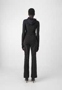 Haut noir ajusté à manches longues avec capuche, associé à un pantalon noir taille haute avec des coutures blanches contrastantes et des jambes évasées.