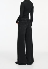 Jean noir à jambes larges avec une taille haute, deux poches arrière et une texture en denim légèrement délavée. Associé à un haut ajusté à manches longues.