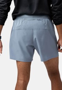 Mäns atletiska shorts i ljusgrått, med ett slätt tyg, elastisk midja och en dragkedjeficka på baksidan. Minimalistisk design.