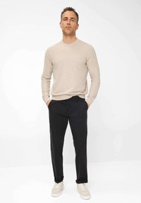 Maglione beige a maglia, pantaloni neri e sneakers chiare. Il maglione ha un collo rotondo e maniche aderenti; i pantaloni hanno un design elegante.