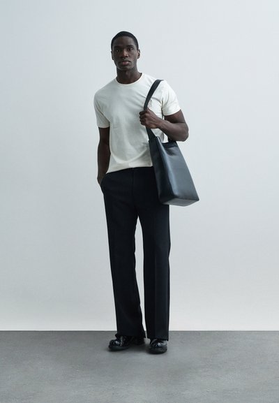 Bolso tote de cuero negro, camiseta crema y pantalones negros a medida. Textura suave, diseño sencillo y detalles mínimos.