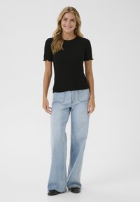 Haut noir à manches courtes côtelé avec bords festonnés, associé à un jean bleu à jambe large, présentant un design classique à cinq poches et un lavage clair.