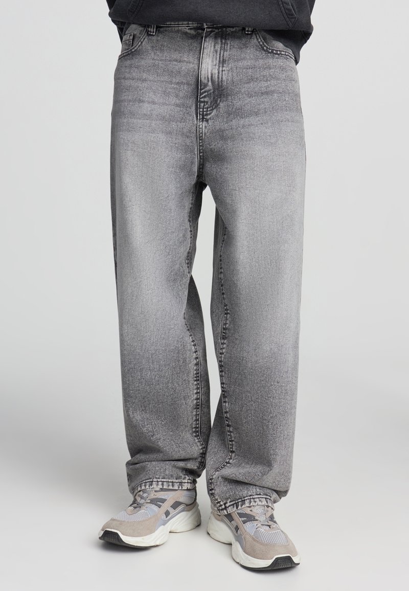 Szare dżinsy o luźnym kroju, z wyblakłym wykończeniem, standardowym pięciokieszeniowym wzorem i przeszyciami wzdłuż szwów.