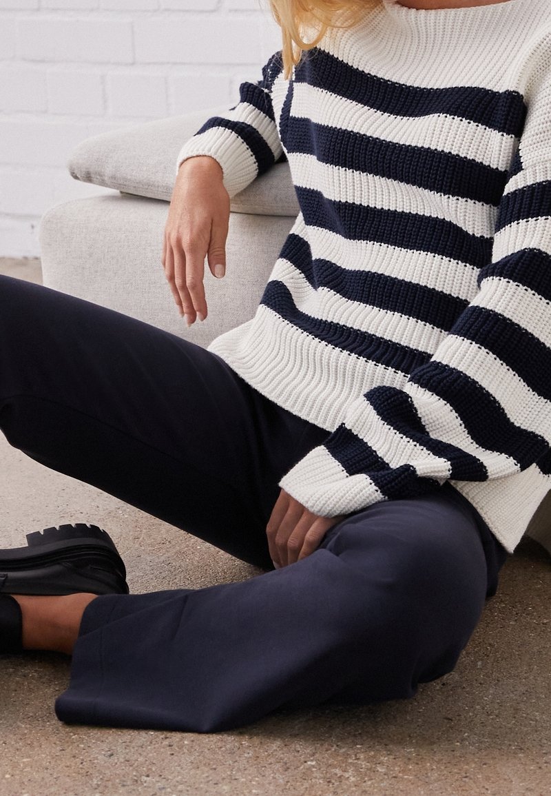Maglione a righe bianco e blu navy, con texture lavorata a maglia, scollo ampio, abbinato a pantaloni blu navy e scarpe slip-on nere.
