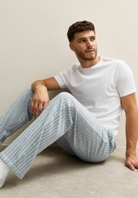 T-shirt blanc à col rond et pantalon de pyjama rayé gris clair, coupe décontractée, avec une texture douce et un design casual.