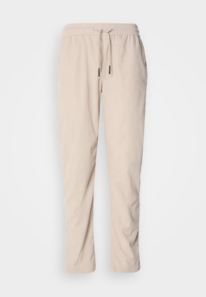 Beige corduroy-housut, joissa on naru vyötäröllä, kapeneva lahkeiden muotoilu ja sivutaskut. Teksturoitu kangas, jossa on pystysuora ribbaus.
