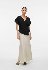 Svart omslagsbluse med korte ermer, prydet med en gullknappdetalj. Kombinert med en gulvlengde beige satengskjørt og olivenfargede flate sko.