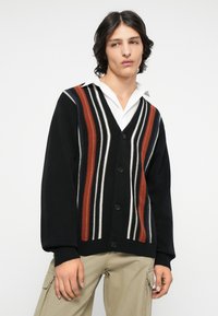Zwarte button-up cardigan met verticale strepen in rood, wit en crème. Gebreide textuur, V-hals ontwerp en geribde manchetten.