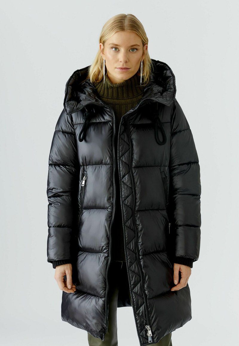 Zwarte pufferjas van glanzend nylon met een capuchon, voorzien van een ritssluiting, een gewatteerd patroon en trekkoorden bij de hals.