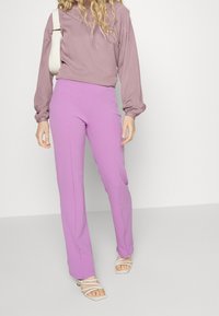 Ljust lila byxor i rak modell, kombinerade med en mauve långärmad topp. Byxorna har en rak bendesign och toppen har en strukturerad axeldetalj.