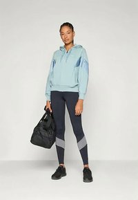 Ανοιχτό μπλε φούτερ με φερμουάρ και γκρι λεπτομέρειες, σε συνδυασμό με ναυτικές κολάν με γκρι ρίγες και μια μαύρη τσάντα duffle. Τα αθλητικά παπούτσια ολοκληρώνουν την εμφάνιση.