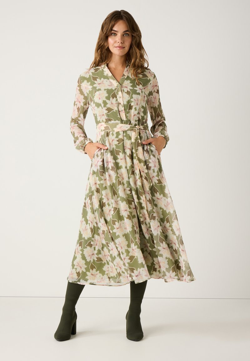Long, floral dress in green with pink accents. Features a button-up front, collar, and pockets. Soft, flowing fabric with a belted waist.