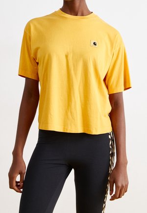 Person wearing a loose yellow short-sleeve shirt with a small logo on chest and black leggings with leopard print side stripes.