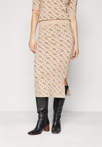 Completo in maglia beige a due pezzi con un motivo testurizzato; top aderente con maniche corte e gonna midi con spacchi laterali, abbinata a stivali neri.