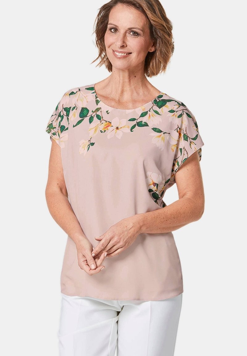 Kurzärmeliges Bluse in pastellrosa mit floralem Muster auf den Schultern. Leichtes Material, lockere Passform mit rundem Ausschnitt. Akzente in Grün und Gelb.