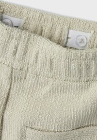 Tessuto beige chiaro con strisce verticali testurizzate, dotato di una vita elastica e di un dettaglio a bottone sull'interno.