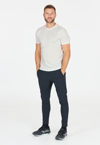 Lys grå kortærmet sports T-shirt, navy slanke bukser og sorte løbesko. Har et subtilt logo på T-shirten og et elegant design.