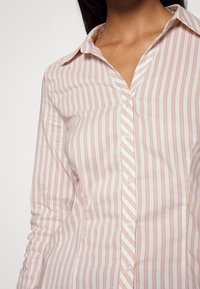 Camicia a righe in morbido cotone. Presenta righe verticali rosa e bianche, colletto classico e bottoni trasparenti.