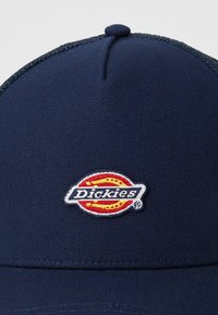 Gorra azul marino con un tejido texturizado, que cuenta con un logo circular bordado de "Dickies" en blanco, rojo y amarillo.