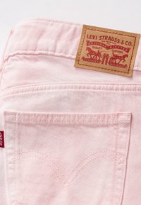 Poche arrière d'un jean Levi's rose pâle avec un artisanat en arc signature et une patch en cuir beige de Levi Strauss & Co. sur la ceinture.