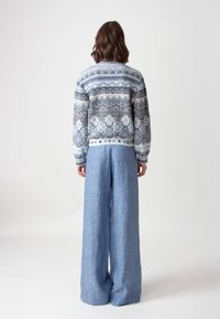 Zila un baltā krāsā adīta džemperis ar sarežģītiem rakstiem, saskaņots ar brīviem gaisiem ziliem lina platām biksēm, redzēts no aizmugures.