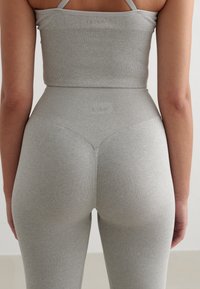 Šedý řasený crop top a legíny s vysokým pasem, bezešvý design, měkká textura, přiléhavý tvar, s logovými detaily poblíž pásku.